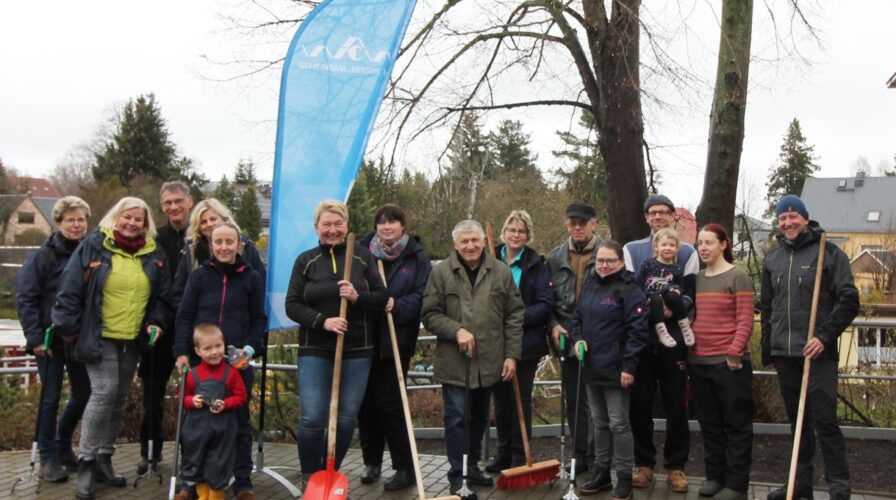 Das Team der WCW und fleißige Helfer beim Gruppenfoto im Rahmen des Frühjahrsputz in Siegmar. Sie halten Besen oder Greifer in den Händen.